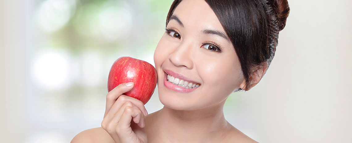 Woman holding an apple with healthy teeth from regular dentist visits at Foothill Dental Care in Livermore